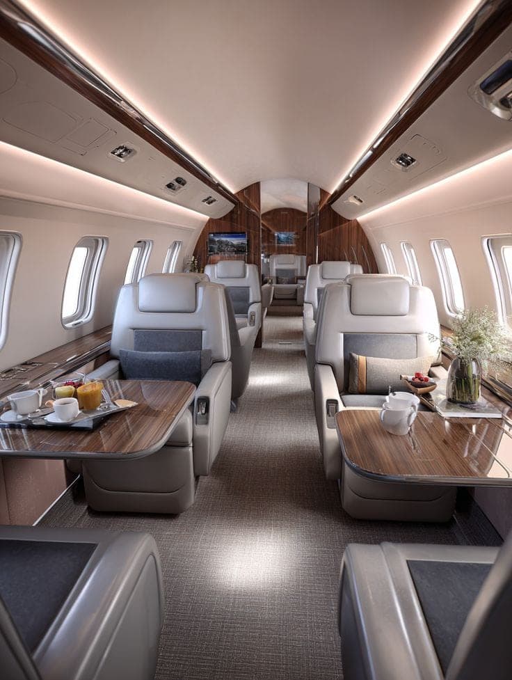 The cabin of a private jet, with facing leather seats and tables set for breakfast
